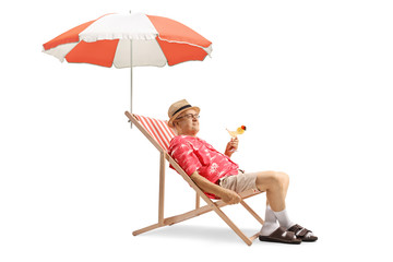 Elderly tourist holding a cocktail and sitting in a deck chair with an umbrella