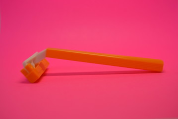 On a bright colorful pink paper background is located and placed a yellow disposable shaving machine