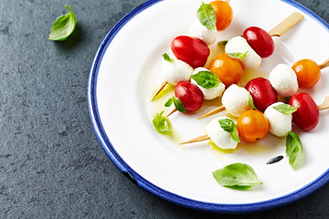 Cherry Tomato and Mozzarella Skewers with basil leaves and olive oil on a plate. Summer snack. Flat lay. Healthy food