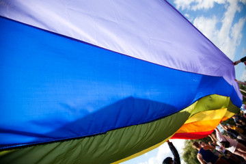 people holding giant rainbow flag at pride parade - LGBT symbol