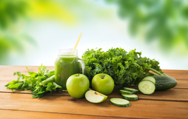 healthy eating, food, dieting and vegetarian concept - close up of glass mug or mason jar with green juice, fruits and vegetables on wooden table over natural background