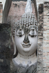 Ancient marvellous stone buddha head statue surrounding by triangle great stone wall at Wat Sri Chum, Sukhothai, Thailand, smilling peace buddism location , travel destination poster backgrounds,