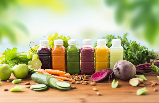 healthy eating, drinks, diet and detox concept - plastic bottles with different fruit or vegetable juices and food on wooden table over green natural background