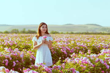 Obraz na płótnie Canvas Beautiful young woman posing near roses in a garden.