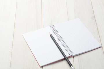 Cuaderno abierto en blanco y lápiz sobre fondo de madera blanca