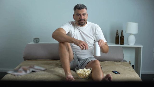 Bachelor spending evening home in front of TV, drinking beer and eating popcorn