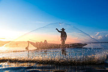 Photo shot of water spatter from fisherman while throwing fishing net on the lake. Silhouette of...