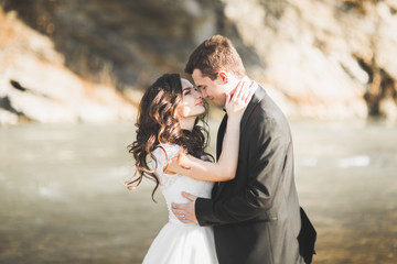 Beautifull wedding couple kissing and embracing near the shore of a mountain river with stones