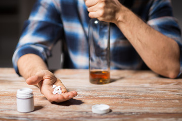 depression, drug abuse and addiction people concept - unhappy drunk man with bottle of alcohol and pills committing suicide by overdosing on medication at night
