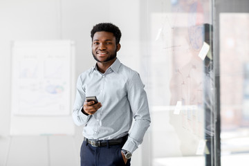 business, people and technology concept - african american businessman with smartphone at office