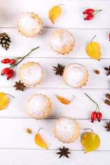 Flat lay in autumn style. Delicious cupcakes with cinnamon sticks, anise stars, berries of rosehip and autumn leaves on white wooden background.
