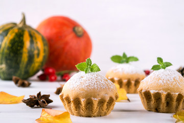 Homemade baking in autumn style. Delicious cupcakes on a wooden board with cinnamon sticks, anise stars, pumpkins and berries of rosehip. On white background.