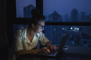 Woman is working with laptop at home during night.