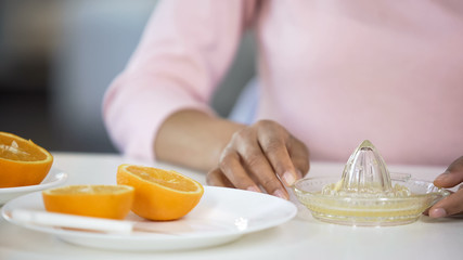 Girl making fresh orange juice, handheld juicer and fruits on table, energy