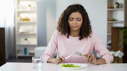 Young woman forcing herself to eat salad, dissatisfaction, weight control diet