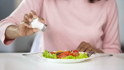 Obraz na płótnie Canvas Woman adding too much salt to her food, unhealthy eating, dehydration problems