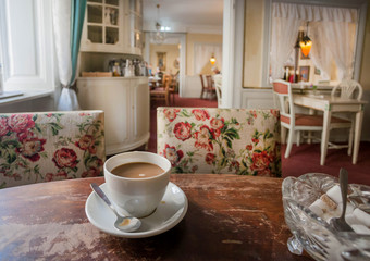 Fototapeta na wymiar Coffee with milk on retro table inside old restaurant, with vintage furniture and cozy rooms of historical home