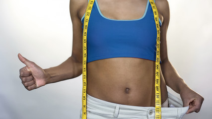 Fit woman wearing oversized pants, showing thumbs-up, weight loss result, diet