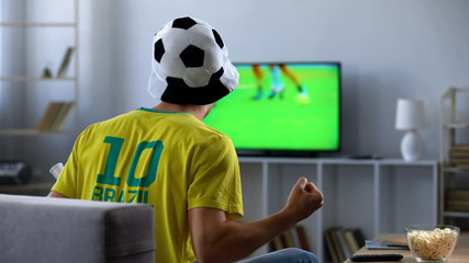 Brazilian team supporter actively cheering favourite football team, match on tv