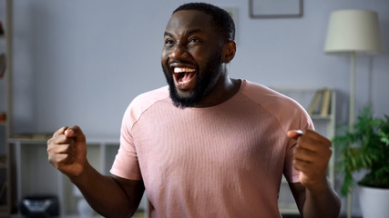 Happy afro-american football fan watching match on tv at home, rejoicing goal
