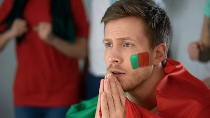 Portugal supporter watching football game on tv, praying for victory, closeup