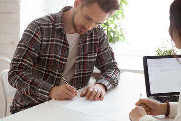 Focused male job candidate signing work contract after successful interview at businesswoman...