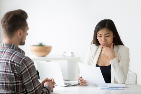 Serious female hr reading job candidates resume, thinking about candidature for open position, thoughtful Asian employer doubting in workers cv, unsure in employment. Bad interview concept