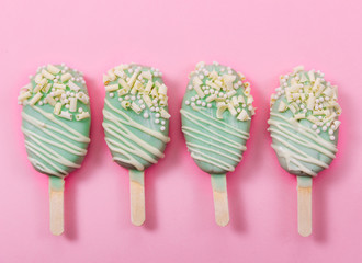 Various cake pops in form of popsicle on stick on pink background.