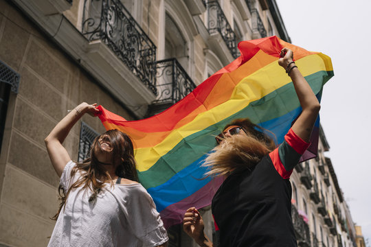 Couple lesbian woman with gay pride flag on the street of Madrid city