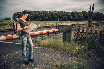 Junge Frau mit Landkarte an einem Bahn&uuml;bergang in der Natur