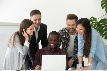 Smiling diverse work team feeling excited reading good online news at laptop on company business success, colleagues happy with online win, shared goal achievement. Concept of cooperation, teamwork