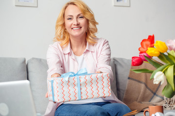 Senior woman at home celebration sitting giving present to camera cheerful