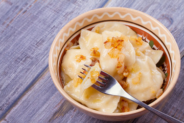 Dumplings, filled with mashed potato - vegetarian dish. Varenyky, vareniki, pierogi, pyrohy in a bowl on wooden table. horizontal
