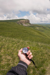 Fototapeta na wymiar A man's hand of a tourist with an authentic compass on the background of a mountain landscape