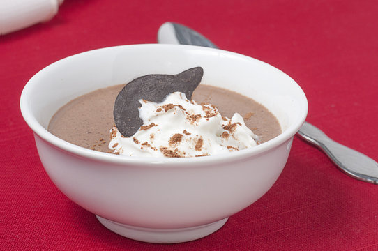 A Dish Of Chocolate Pudding And Spoon, Topped With A Dollop Of Whipped Cream And Garnished With Powdered Cocoa Powder And A Chocolate Wafer.