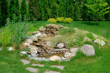 Rockary in the form of a mountain waterfall in the garden with stones and many different flowers and plants