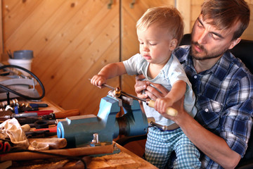 Father teaches his toddler son to use tools vise and rasp in a workshop. Cute boy exploring new stuff. Fatherhood concept