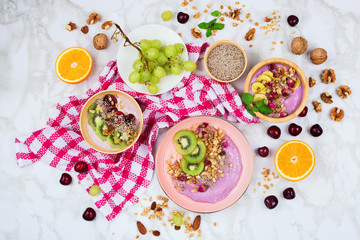 Flatlay with healthy vegan breakfast arrangement on marble background. Coconut and wooden bowls with smoothies, plant based yogurt, chia seeds and other ingredients