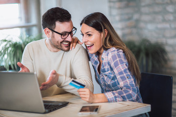Smiling couple using digital tablet and credit card at home