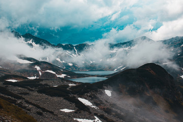 Two large lakes surrounded by mountains covered with snow in fog against the blue sky