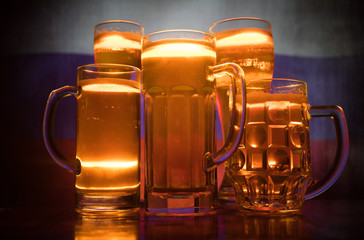Creative concept. Beer glasses on table at dark toned foggy background with blurred view of flag of Russia. Support your country with beer concept.