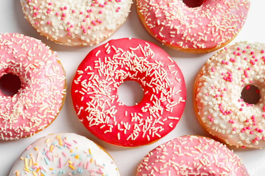 Delicious glazed doughnuts with sprinkles on light background, top view
