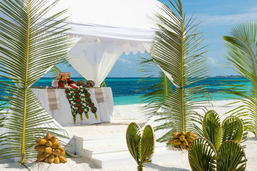 Hochzeitstisch unter weißem Zelt an weißem Strand und türkisem Meer mit Palmzweigen
