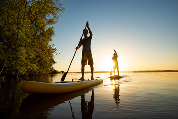 Men, friends sail on a SUP boards in a rays of rising sun