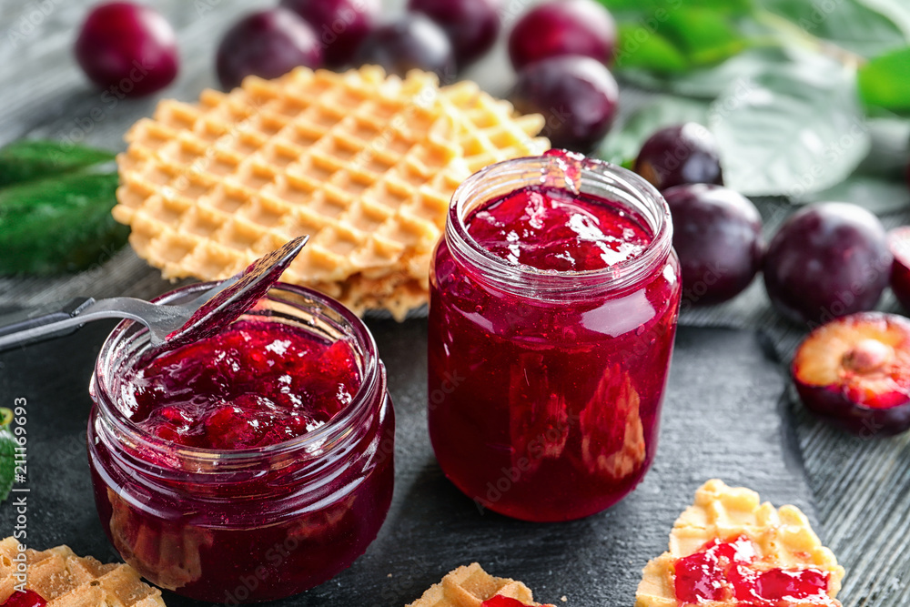 Sticker Glass jars with delicious homemade plum jam on table