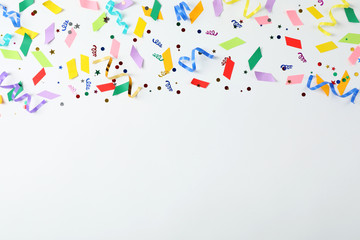 Colorful confetti and streamers on white background, top view