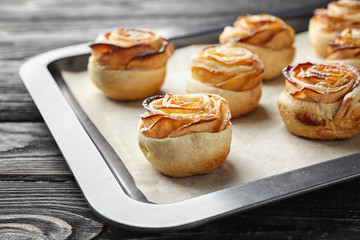 Baking tray with apple roses from puff pastry on wooden background, closeup