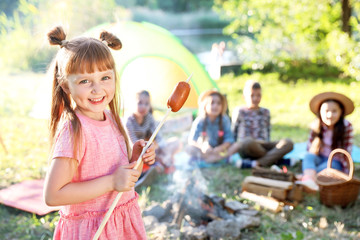 Little girl with fried sausage outdoors. Summer camp