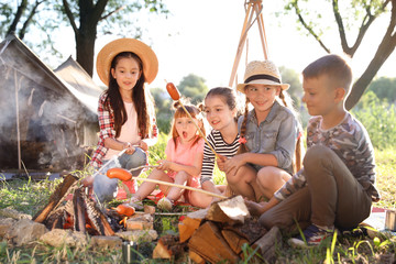 Little children frying sausages on bonfire. Summer camp