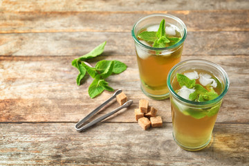 Glasses with aromatic mint tea, fresh leaves and sugar cubes on wooden table